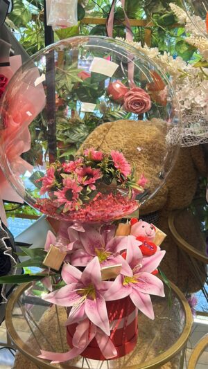 Pembe çiçekler ve çerçeveli dekoratif sunum; şeffaf balon, kırmızı küçük çiçekler ve pembe peluş detay